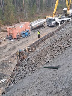 Työmaa: Miehiä työskentelemässä kivirakenteiden parissa, taustalla nosturi ja kuorma-auto.