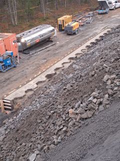 Rakennustyömaa, jossa on jyrkkä kivirinne, koneita ja säiliöauto.