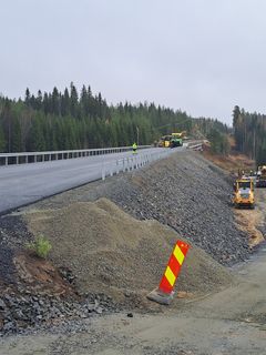 Tietyömiehiä ja ajoneuvoja uudella siltatyömaalla, ympärillä metsää.