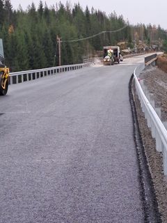Tietyömiehet työskentelevät juuri päällystetyllä maantiellä, mukana on tienvierustalla oleva kaide.