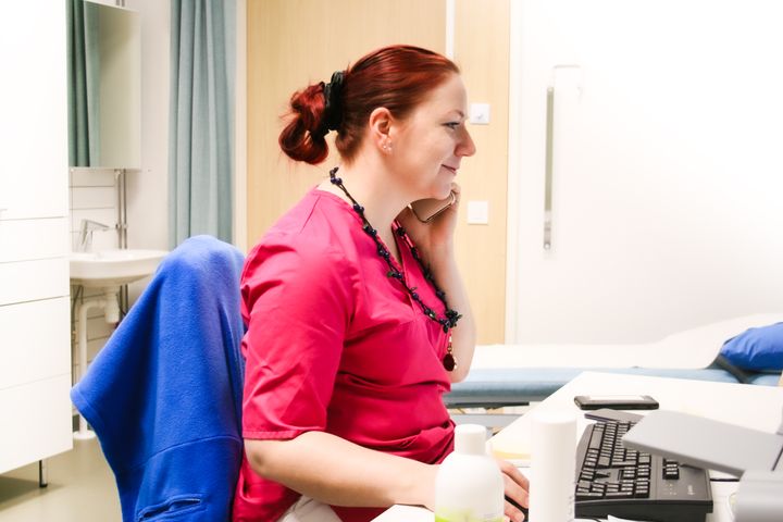 Nainen istuu tietokoneen ääressä puhelin korvallaan.