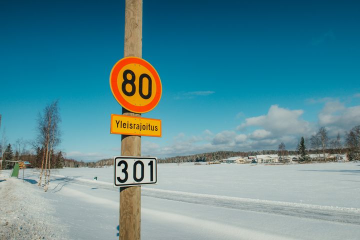 Kevättalvinen aurinkoinen kuva, etualalla 80 nopeusrajoitus liikennemerkki, taustalla luminen aukea ja sininen taivas