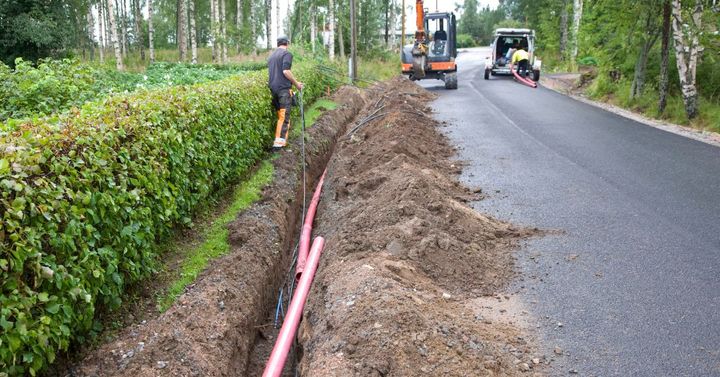 Mies vetää putkea ojaan. Kaksi autoa.