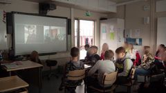 Elever sitter i klassrummet och tittar på skärmen. På skärmen finns det jordbrukare som jobbar.