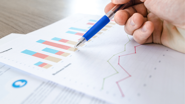 En person pekar på ekonomiska diagram och statistik på papper.