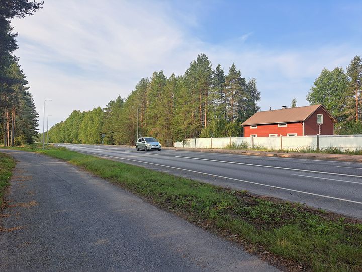 Kevyenliikenteen väylä ja auto ajamassa valtatiellä, aidan takana talo.