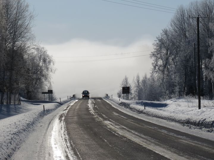 Talvisella maantiellä yksittäinen auto aurinkoisella ilmalla.