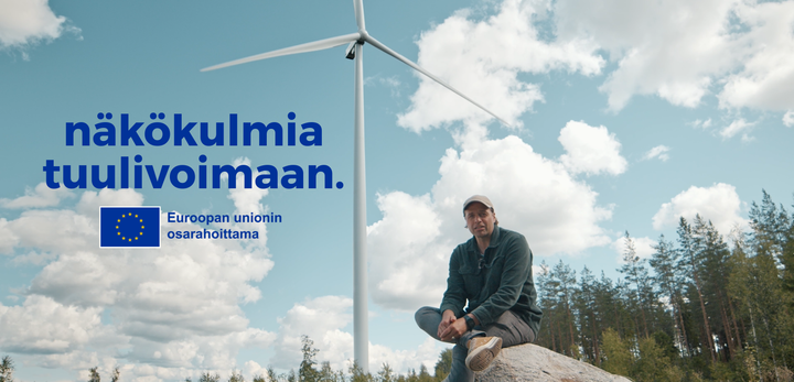 Mies katsoo kameraa tuulivoimala takana.