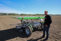 Juha Jarttu seisoo peltorobotin vieressä pellolla.