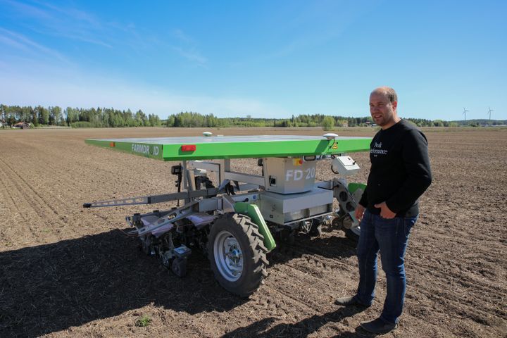 Juha Jarttu seisoo peltorobotin vieressä pellolla.