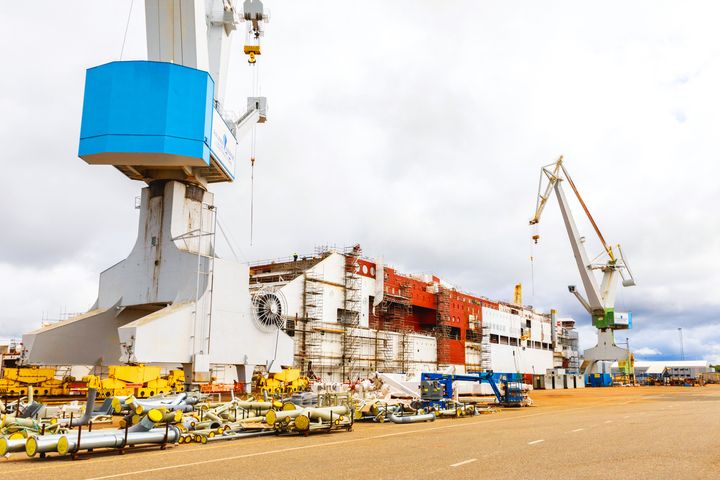 Kaksi nosturia ja keskellä keskeneräinen laiva telakalla.