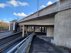 Alt text: Betoninen ylikulkusilta kulkee autotien ja junaradan yli.