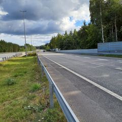 Moottoritie metsämaisemassa, jossa näkyy pilvinen taivas ja kaiteet molemmilla puolilla.