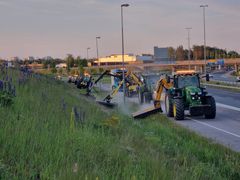 Traktorit ajavat moottoritien viereistä tietä leikkaamassa tien pientareen ruohoa.