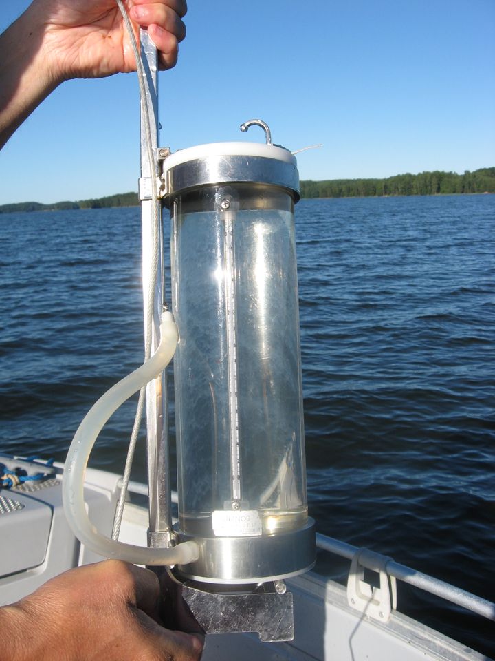 En person håller en vattenprovtagare och termometer över vattenytan på en sjö.