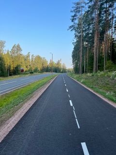 Nybyggd gång- och cykelväg omgiven av skog och en parallell bilväg.