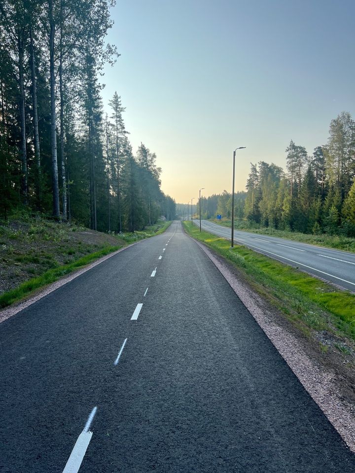 Alt-teksti: Asfaltilla päällystetty jalankulku- ja pyörätie kulkee metsän reunustamana ajoradan vieressä.