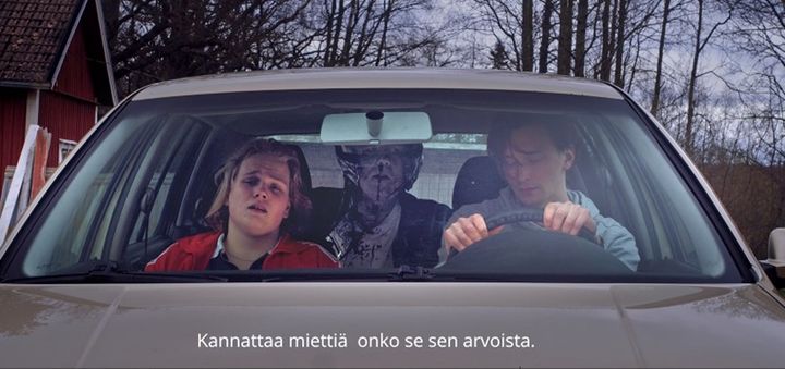 Kuvakaappaus videosta. Kaksi nuorta istuu auton etupenkillä peloissaan. Takana verinen mies katsoo nuoria varoittaen. Alla teksti "Kannattaa miettiä, onko se sen arvoista."