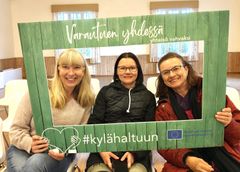 Kolme ihmistä poseeraa kuvakehyksen kanssa.