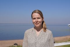 Johanna Mattila ulkona vaaleassa paidassa. Taustalla näkyy meri.