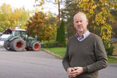 Tauno Linkoranta ulkona. Taustalla näkyy traktori ja ruskan väreissä olevia puita.