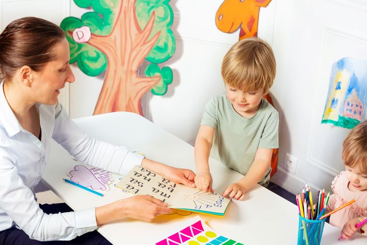 Nainen auttaa pieniä lapsia opettelemaan kirjaimia