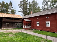 Punainen perinteinen puutalo ja vanha puinen rakennus kesäisessä pihapiirissä.