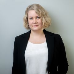 Kuvassa kameralle hymyilevä vaaleatukkainen nainen