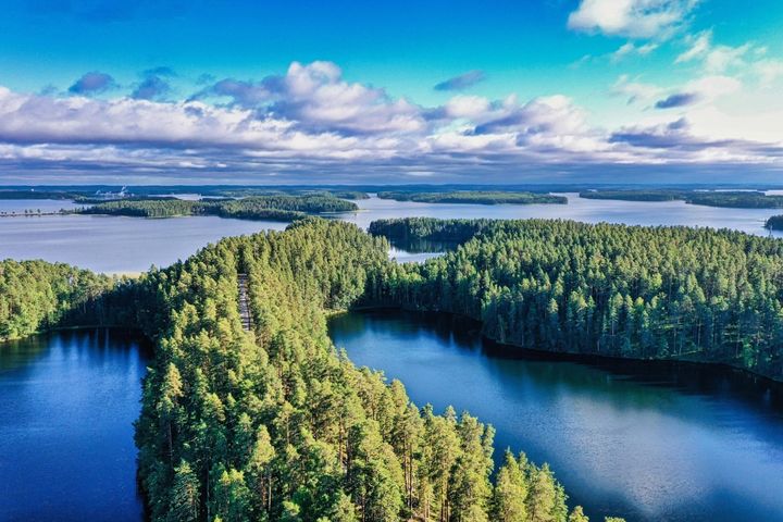 Ilmakuva järvimaisemasta, jossa sinistä vettä ja vihreiden metsien peitossa olevia saaria. Horisontissa pilviä.
