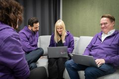 Kuvassa on neljä Maanmittauslaitoksen työntekijää, joilla on violetit hupparit. Yhdellä on sylissä kannettava tietokone.