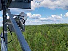 Pieni metallinen laite kiinnitettynä telineeseen metsän reunassa