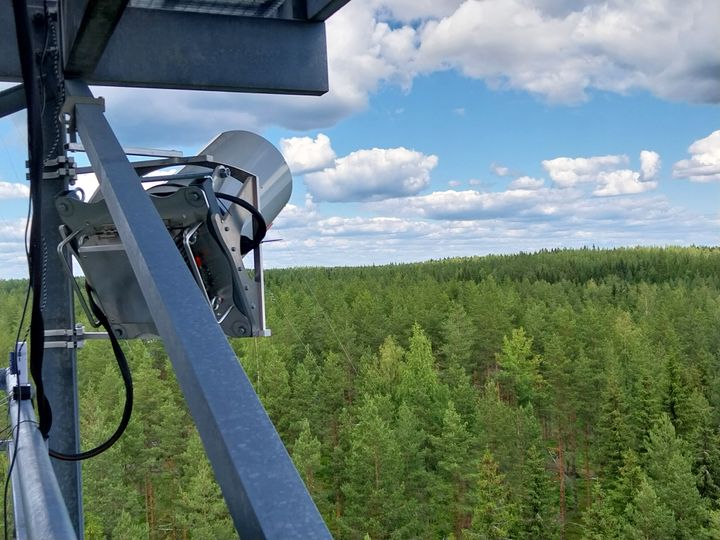 Pieni metallinen laite kiinnitettynä telineeseen metsän reunassa