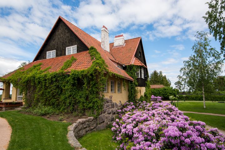 Vanha%20Hvittr%E4skin%20rakennus%20Kirkkonummella%2C%20sen%20katolla%20punaiset%20kattotiilet%20ja%20seinill%E4%20vihre%E4%E4%20k%F6ynn%F6st%E4.%20Etualalla%20kukkiva%20purppura%20rodopenkki.