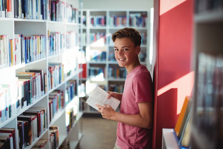 Glad pojke som läser en bok i biblioteket.