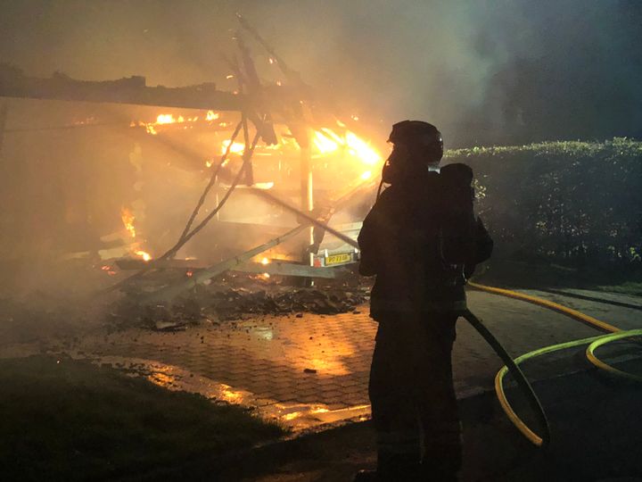 En brandman står framför ett brinnande hus på natten.