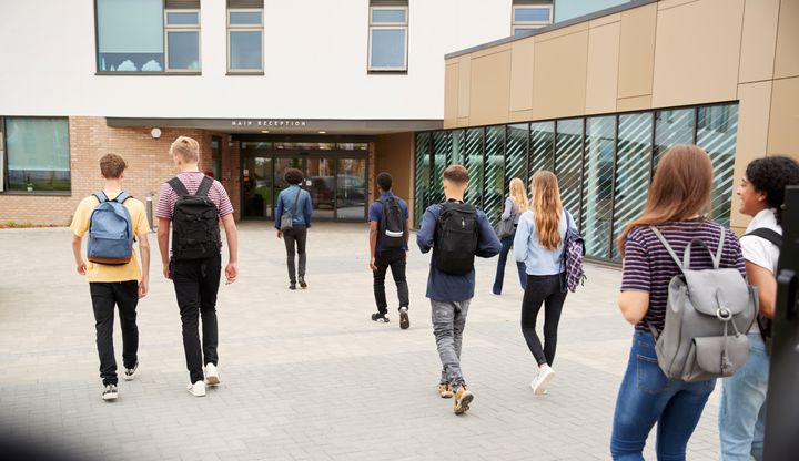 Joukko nuoria kävelee kohti koulun pääsisäänkäyntiä.