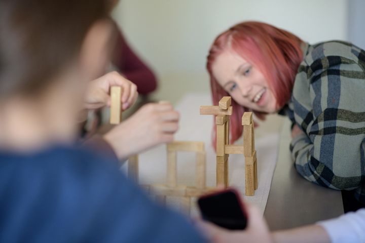 Nuori tyttö katsoo rakennuspalikoista tehtyä rakennelmaa ja hymyilee, kuvituskuva.