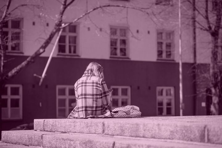 Yksinäine nuori istuu kaupunkiympäristössä selin kameraan
