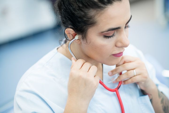 Nainen työvaatteissa kuuntelee stetoskoopilla.