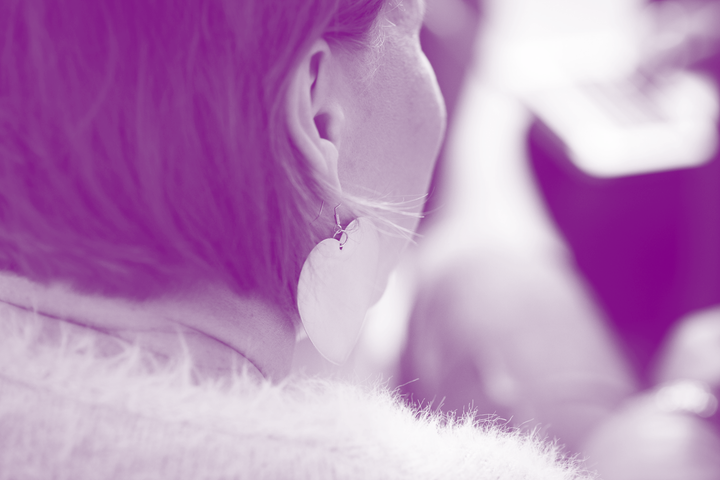 Henkilön lyhyet hiukset ja suuret sydämenmuotoiset korvakorut, violetti sävymaailma.