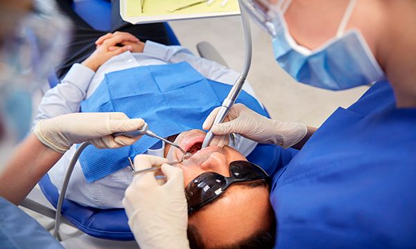 Hammaslääkäri hoitaa potilasta, joka makaa hammaslääkärin tuolissa suojalasit päässä.