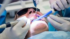 Hammaslääkäri hoitaa potilasta, jolla on aurinkolasit päässä, ja käyttää erilaisia hammashoitovälineitä.