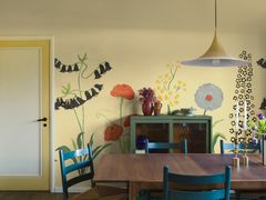 Ruokailutila, jossa vihreä vitriini, tumma ruokapöytä ja siniset tuolit. Seinällä keltapohjainen tapetti, jossa isoja kukkia.