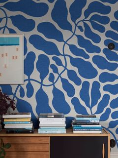 Sininen lehtikuvioiden tapetti, jonka edessä kirjoituspöytä ja 3 pinoa kirjoja.