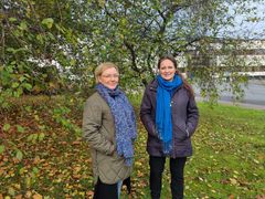 Hanna ja Ilse seisovat kädet taskuissa syksyisen lehtipuun alla ja hymyilevät.