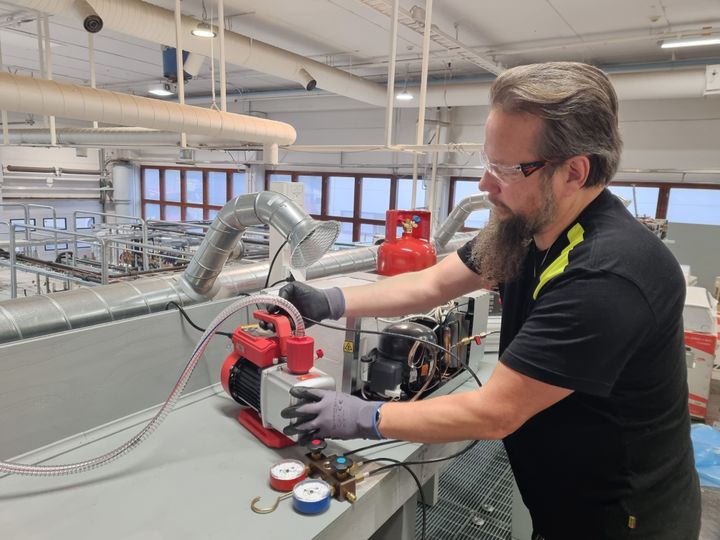 Kouluttaja työskentelee teollisuuskeittiön kylmälaitteiden parissa valoisassa harjoitustilassa.