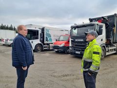 Kaksi miestä keskustelee pysäköityjen kuorma-autojen edessä ulkona.