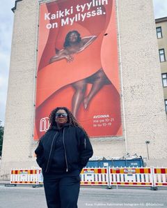 Nainen seisoo ison mainoslakanan, jossa on hänen oma kuvansa, edessä.