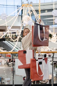 Hymyilevä nainen esittelee kahta kestokassia, taustalla näkyy kauppakeskuksen liukuportaita ja jouluvaloja.
