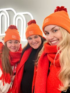 Kolme naista hymyilee kameralle oranssit pipot päässä.